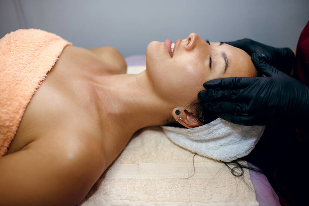 Close-up of young woman receiving facial massage at beauty spa. Side view of modern cosmetology skin and body care - Φωτογραφία, εικόνα