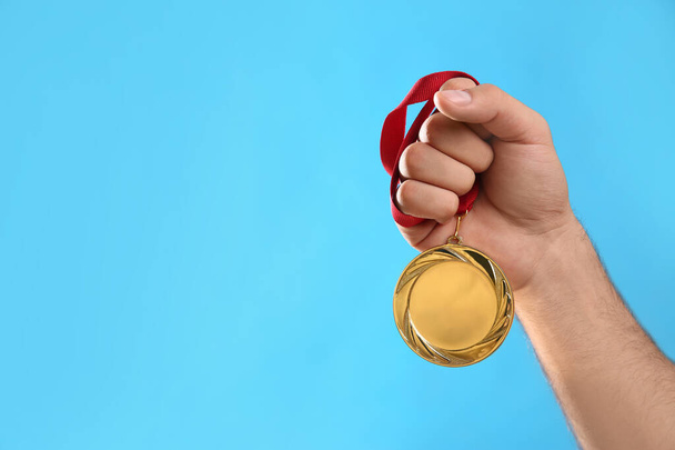 Man holding golden medal on light blue background, closeup. Space for design - Foto, immagini