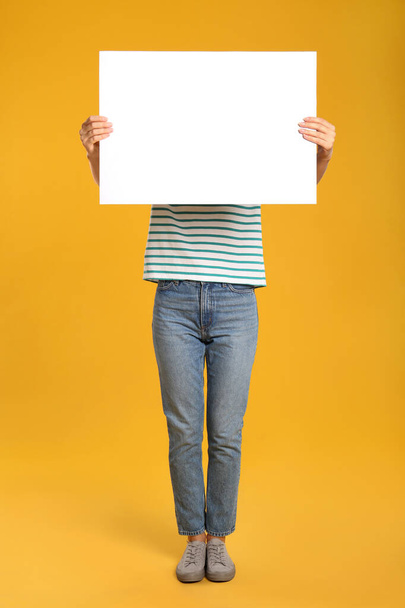 Woman holding white blank poster on yellow background. Mockup for design - Foto, immagini