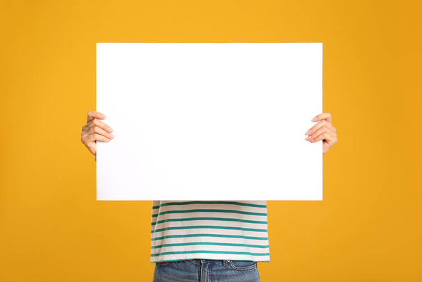 Woman holding white blank poster on yellow background. Mockup for design - Foto, imagen