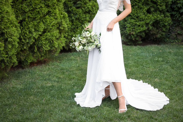 Bride in beautiful wedding dress with bouquet outdoors, closeup - Foto, imagen