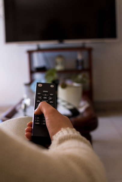 Girl sitting on a sofa with a black tv remote controler at home - Photo, image