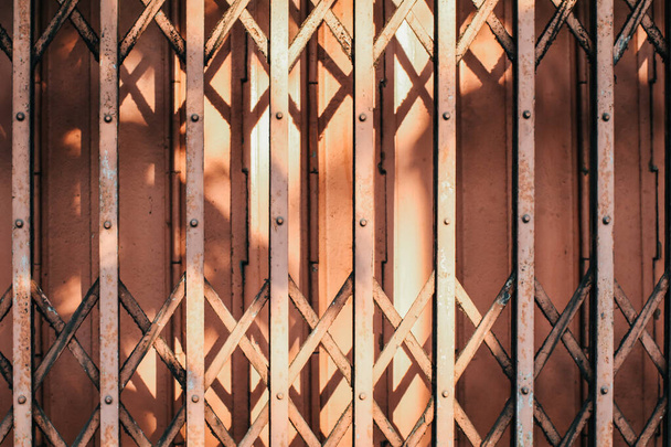 Morning sunlight and shadow on the closed metal steel door - Folding door texture pattern and background.Expanded metal sliding gate. Old style grunge metal door. - Fotó, kép