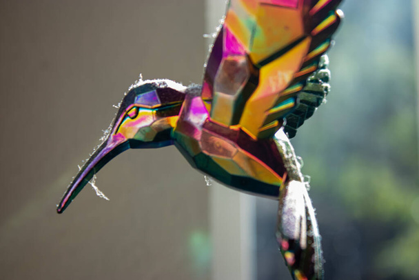 Polvorienta figura de cristal de ave tarareando colgando a la luz del sol - Foto, imagen