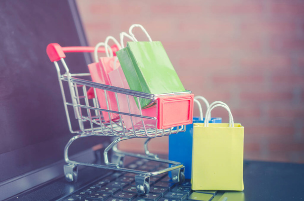 Barevné papírové nákupní tašky v nákupním košíku na klávesnici notebooku, e-commerce nebo elektronickém obchodu je transakce nákupu nebo prodeje zboží nebo služeb on-line přes internet. - Fotografie, Obrázek