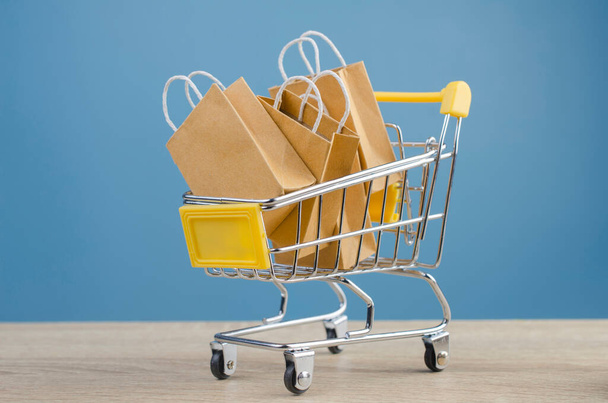 Bolsas de compra de papel en un carrito de la compra en la mesa de madera, comercio electrónico o comercio electrónico es una transacción de compra o venta de bienes o servicios en línea a través de Internet. - Foto, imagen