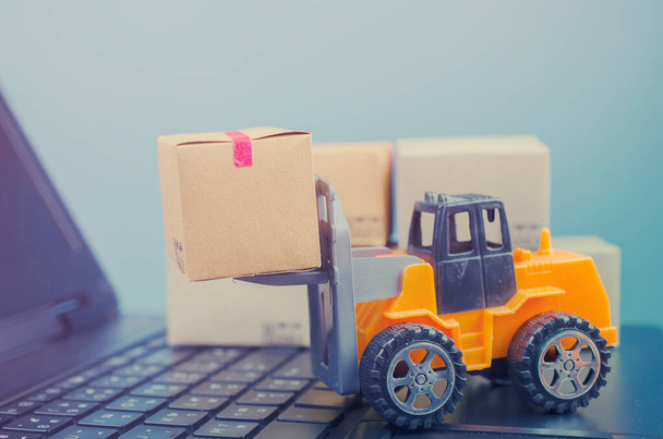 Forklift truck with boxes on a laptop keyboard,e-commerce or electronic commerce is a transaction of buying or selling goods or services online over the internet. - Photo, Image