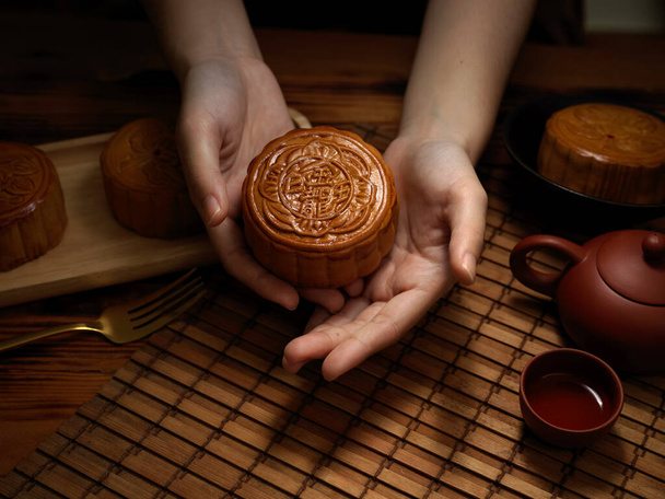 Detailní pohled na ženské ruce držící měsíční dort nad stolem při měsíčním festivalu. Čínský znak na měsíčním dortu představuje "pět jader a pečené vepřové" v angličtině - Fotografie, Obrázek