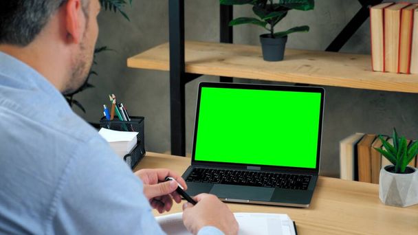 Hombre profesor en casa oficina se sienta mesa con la pluma en la mano con el ordenador portátil de pantalla verde - Foto, Imagen