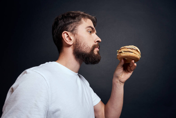 Férfi eszik hamburger gyorsétterem Gourmet étkezési sötét háttér - Fotó, kép