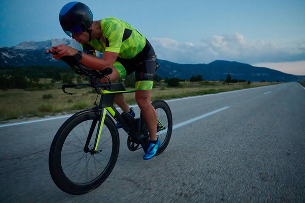 triathlon athlete riding professional racing bike at night workout on curvy country road w - Foto, imagen
