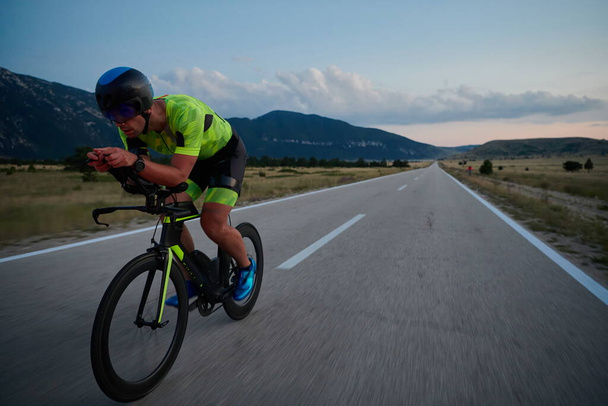 triathlon athlete riding professional racing bike at night workout on curvy country road w - Foto, afbeelding