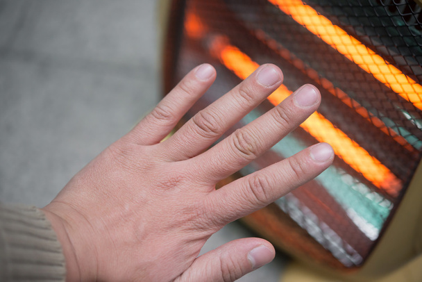 Aquecendo uma mão na frente de um aquecedor elétrico
 - Foto, Imagem