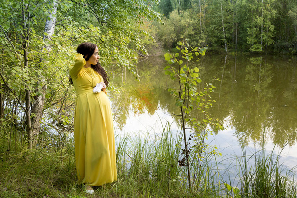 Portrait of a pregnant woman in a yellow dress in the autumn forest - Photo, Image