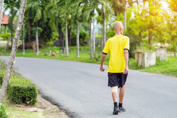 Widok z tyłu Portret Azjaty w stroju fitness spacerującego i biegającego dla dobrego zdrowia w parku publicznym. Starszy jogger w naturze. Starszy człowiek cieszący się spokojną naturą. Koncepcja opieki zdrowotnej. - Zdjęcie, obraz