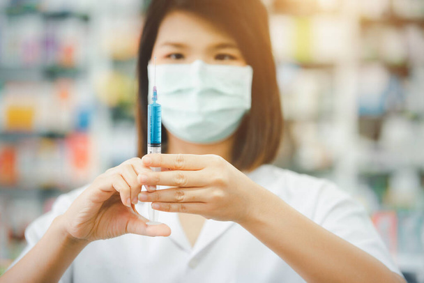 Yüz maskesi takan güzel Asyalı doktor kadının portresi bulanık arka planda hastane ya da klinikte aşı şırıngası kullanılıyor. - Fotoğraf, Görsel