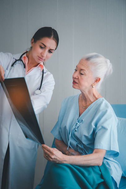 Naislääkäri näyttää röntgenkuvauksen tulos ja selittää terveysongelmia iäkkäille naisille potilaan huoneessa sairaalassa. Terveydenhuollon kotihoidon käsite - Valokuva, kuva