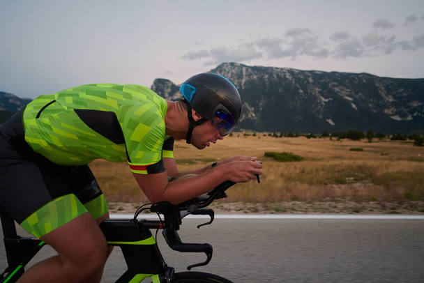 триатлон атлет верховая езда профессиональный гоночный велосипед на тренировке на извилистой дороге страны - Фото, изображение