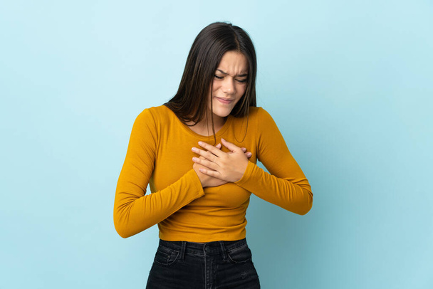 Teenager girl isolated on blue background having a pain in the heart - Valokuva, kuva