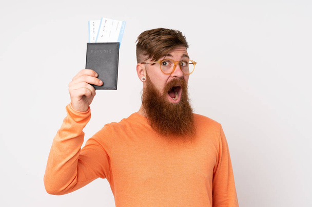 Рыжий с длинной бородой на изолированном белом фоне счастлив в отпуске с паспортом и билетами на самолет - Фото, изображение