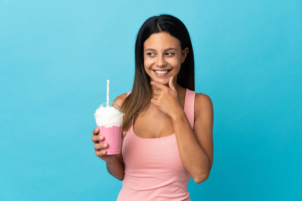 Молодая женщина с клубничным молочным коктейлем смотрит в сторону и улыбается - Фото, изображение