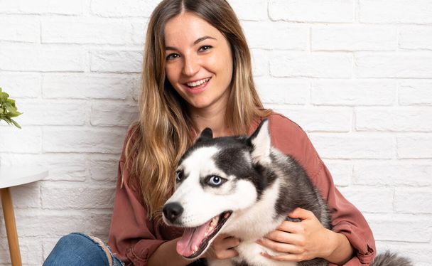 Young pretty woman with her husky dog sitting in the floor at indoors - Foto, Imagen