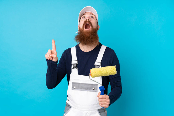 Homem pintor com barba longa sobre fundo azul isolado apontando com o dedo indicador uma ótima ideia - Foto, Imagem