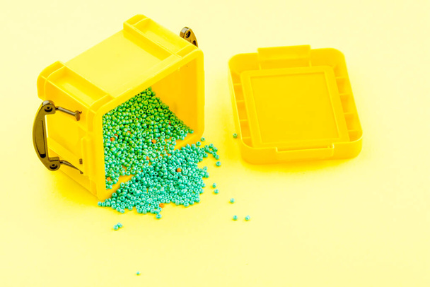 siniset helmet kaadetaan keltaisesta muovisäiliöstä keltaiselle pinnalle. vuotopitoisuus - Valokuva, kuva