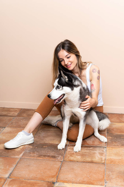 Giovane bella donna con il suo cane husky seduto nel pavimento al chiuso - Foto, immagini