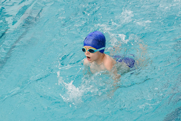 vista superior de un niño de 7 años jugando y nadando en la piscina - Foto, Imagen