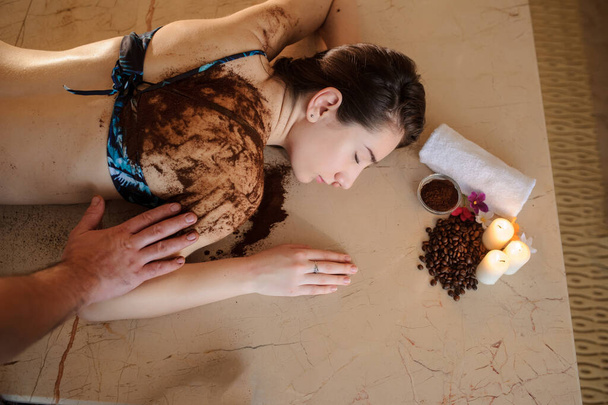 вид збоку красивої жінки в спа-салоні, що має спа-терапію з кавою, зробленою масажистом
  - Фото, зображення