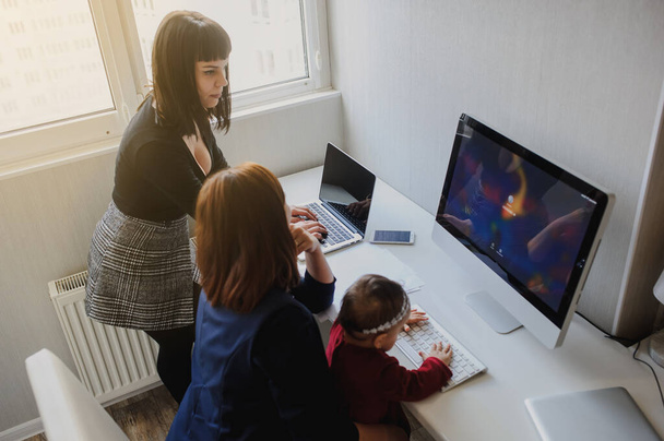 крупним планом фото двох жінок в офісному вбранні, що працюють на комп'ютерах і обговорюють звіт; одна з них з дівчинкою на руках
 - Фото, зображення