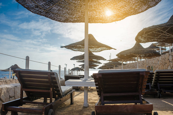 Sombrillas y tumbonas de paja en una playa en un idílico complejo tropical para unas vacaciones de verano - Foto, Imagen