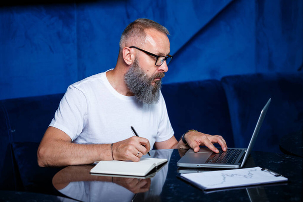 Mentore maschio adulto, regista, uomo d'affari con gli occhiali e un vestito che studia i documenti mentre siede al tavolo. Concetto giorno lavorativo - Foto, immagini