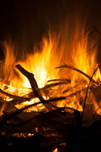 Огненное пламя, жгущее дерево в ночь. Это горячее светящееся тело воспламененного газа, которое генерируется чем-то в огне.. - Фото, изображение