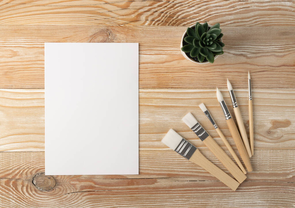 Mockup artista minimale con pennelli su tavolo in legno piatto lay e vista dall'alto. Carta bianca modello su sfondo, cornice pittore con spazio di copia - Foto, immagini