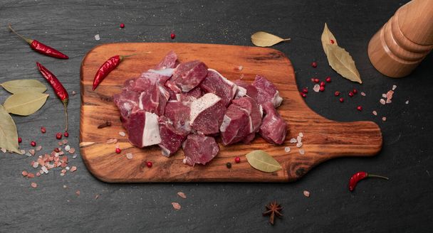Raw chopped lamb fillet, diced tenderloin or cubed mutton sirloin meat on black stone plate background. Fresh sheep fillet, loin filet with spices on wood board top view - Photo, Image