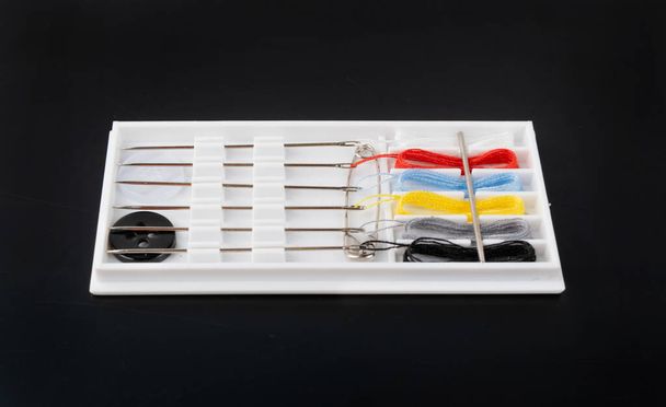 Pequeño kit de costura con agujas, hilos multicolores, pin y botones. Kit de viaje de costura o caja de hotel sobre fondo negro - Foto, Imagen