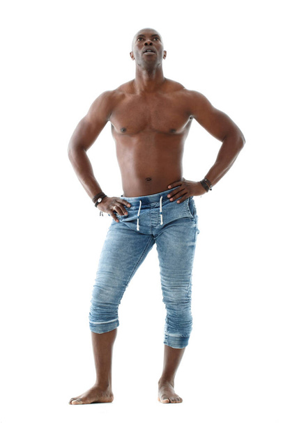 Athletic young black man in jeans and with a nude torso is standing in full growth isolated on white background. - Fotó, kép