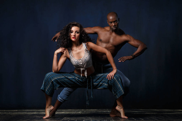 A slender white girl and an athletic black man in a graceful dance against a dark blue background. - Photo, image