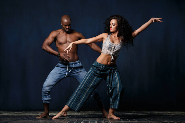 A slender white girl and an athletic black man in a graceful dance against a dark blue background. - Фото, изображение