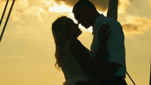 Két szerelmes fekete sziluettje. Friss házasok naplementekor. A vőlegény megcsókolja a menyasszonyt, és gyengéden megöleli naplementekor. - Felvétel, videó