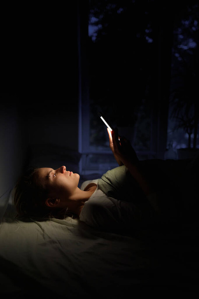 A young girl lies in bed and looks at her smartphone - Foto, imagen