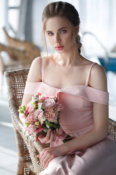 美しいです若いですピンクのドレスに花束で彼女の手はプールの近くのウィッカーチェアに座っています. - 写真・画像