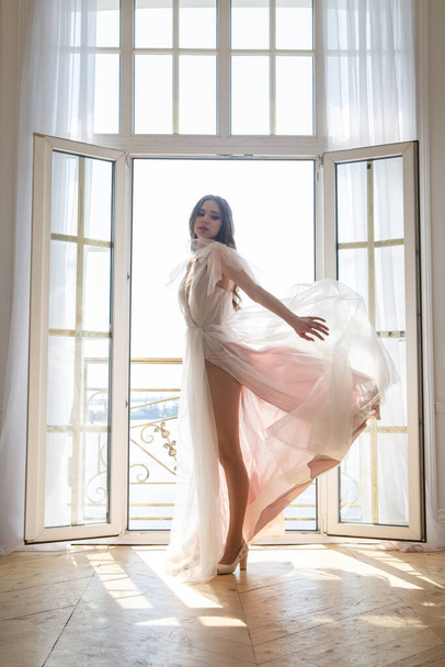 窓の後ろに流れるドレスに細い花嫁の繊細なシルエット. - 写真・画像