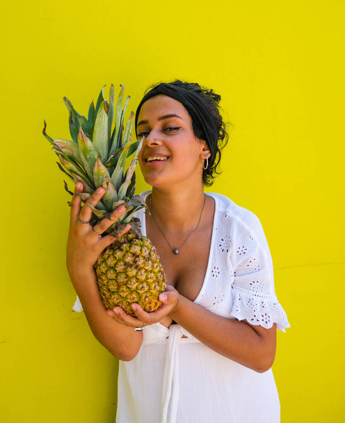 attractive Brazilian female with pineapple on yellow background.  attractive Brazilian female with pineapple and juice on yellow background - Фото, изображение