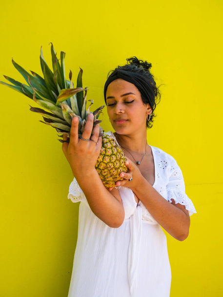 fêmea brasileira atraente com abacaxi no fundo amarelo. fêmea brasileira atraente com abacaxi e suco no fundo amarelo - Foto, Imagem