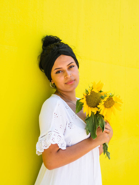 Sarı arka planda ayçiçekleri olan çekici Brezilyalı kadın. Parkta ayçiçekleri olan çekici Brezilyalı kadın. - Fotoğraf, Görsel
