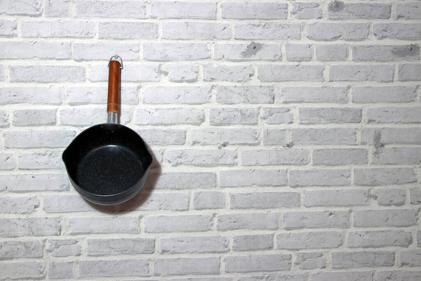 Vařit hrnec s dlouhou dřevěnou rukojetí visí na zdi cihlový vzor. - Fotografie, Obrázek