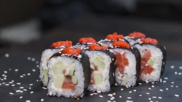 Set de rollos de sushi con atún, salmón, pepino, aguacate sobre mesa giratoria sobre fondo negro primer plano. Surtido de comida japonesa en restaurante. - Metraje, vídeo